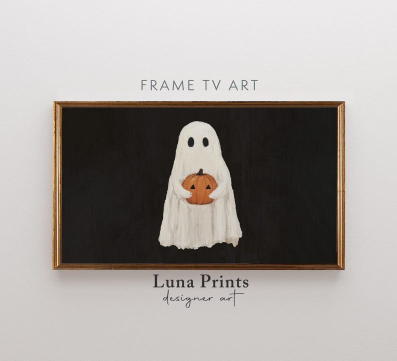 May include: A framed digital art print featuring a white ghost holding an orange pumpkin against a black background. The artwork has a vintage, textured appearance. The frame is a warm brown color. The text "FRAME TV ART" and "Luna Prints designer art" are visible.