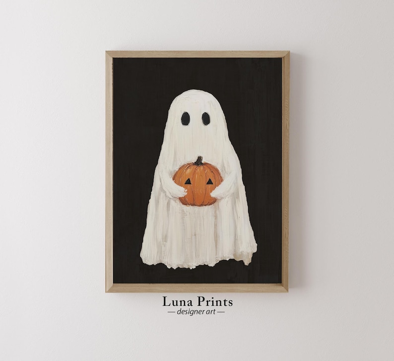 Peut inclure: Un fant&ocirc;me blanc tenant une citrouille orange sculpt&eacute;e sur un fond noir. L'image est encadr&eacute;e dans un cadre en bois brun clair. Le texte "Luna Prints - designer art" est sous le cadre.