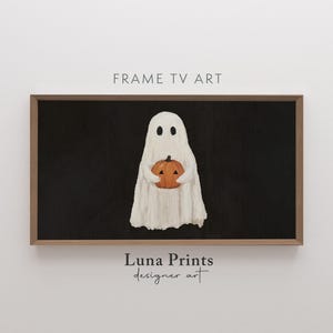 May include: A framed digital art print featuring a white ghost holding an orange pumpkin against a black background. The artwork is labeled "Frame TV Art" and "Luna Prints designer art". The overall theme is Halloween.