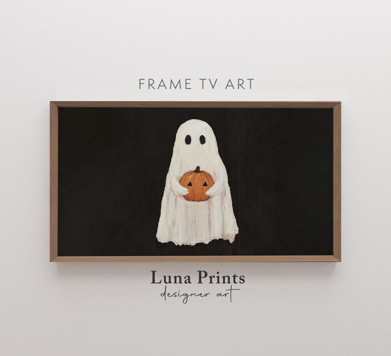 May include: A framed digital art print featuring a white ghost holding an orange pumpkin against a black background. The artwork is labeled "Frame TV Art" and "Luna Prints designer art". The overall theme is Halloween.