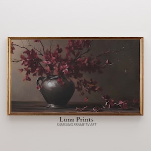 May include: A framed painting depicting a dark grey vase filled with burgundy flowers. The vase has two handles and rests on a wooden table. The painting is titled "Luna Prints" with the text "SAMSUNG FRAME TV ART" beneath the title.
