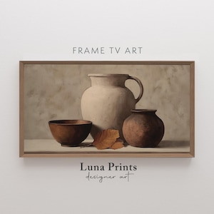Può includere: Stampa incorniciata di una natura morta con una grande brocca beige con manico, una brocca marrone più piccola e una ciotola di legno. Alcune foglie marroni sono davanti alle brocche. Il testo "FRAME TV ART" e "Luna Prints designer art" sono visibili.