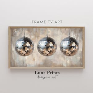 May include: A framed print featuring three hanging disco balls. The disco balls are silver and reflective, set against a neutral-toned abstract background. The words "FRAME TV ART" are at the top.