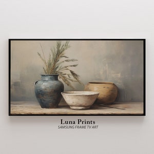 May include: A framed print featuring a still life composition. It showcases a blue vase with dried plants, a cream-colored bowl, and a tan-colored pot. The artwork has a muted color palette and a rustic aesthetic. The text "Luna Prints" and "SAMSUNG FRAME TV ART" is visible.