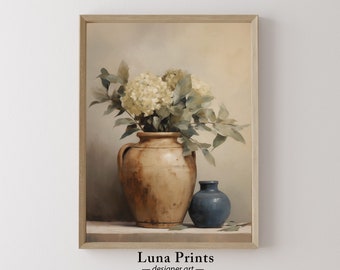 May include: A framed art print featuring a still life composition. A large, aged brown vase holds white flowers and green foliage. A small blue vase sits beside it. The artwork is signed "Luna Prints - designer art -."
