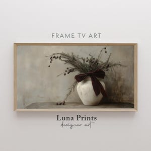 May include: A framed print of a still life featuring a white ceramic vase with a burgundy ribbon, filled with dried greenery and berries. The background is a muted beige with a wooden surface.