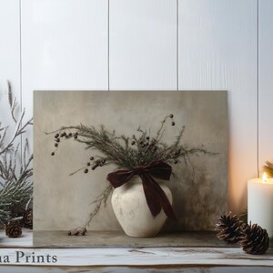 May include: A white ceramic vase with a burgundy velvet bow sits on a wooden shelf. The vase is filled with dried branches and berries. The background is a white wall with a wood grain texture.