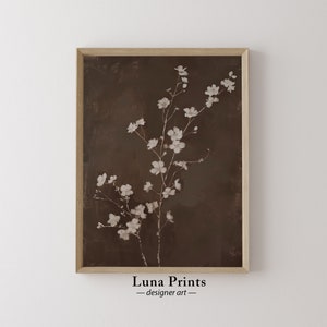 Puede incluir: Una impresión enmarcada de una rama de flores blancas sobre un fondo marrón. La impresión se titula "Luna Prints - designer art".