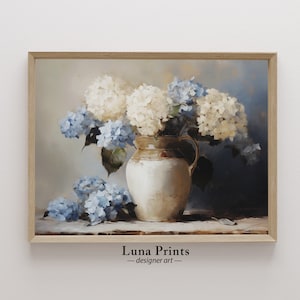 May include: A painting of a white ceramic pitcher filled with a bouquet of white and blue hydrangeas. The flowers are arranged in a vase with a brown rim and a light brown background. The painting is framed in a light wood frame.