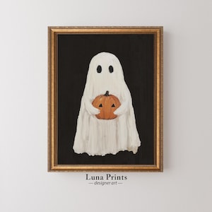 以下が含まれることがあります： 黒い背景に、オレンジ色のカボチャを手にした白い幽霊。金色の額縁で飾られています。