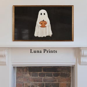 May include: A framed Halloween-themed artwork featuring a white ghost holding an orange pumpkin against a black background. The artwork is in a gold frame and is displayed above a white mantelpiece. The text "Luna Prints" is below the artwork.