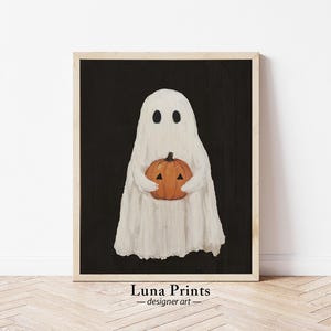 Peut inclure: Un fant&ocirc;me blanc tenant une citrouille orange en forme de jack-o'-lantern sur un fond noir. Le fant&ocirc;me a deux yeux noirs et un corps blanc en forme de drap. La citrouille a un visage sculpt&eacute; avec un nez triangulaire et deux yeux triangulaires. L'image est encadr&eacute;e dans un cadre en bois.