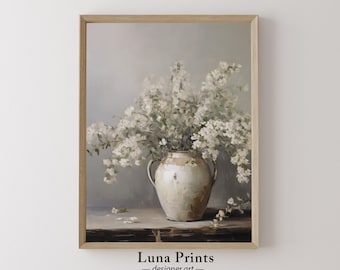May include: A white ceramic vase with a rustic finish filled with white flowers. The vase has two handles and is sitting on a wooden table. The background is a light gray.