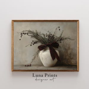 May include: A white ceramic vase with a burgundy velvet bow sits on a wooden surface. The vase is filled with dried branches with small, dark berries. The background is a light gray wall.