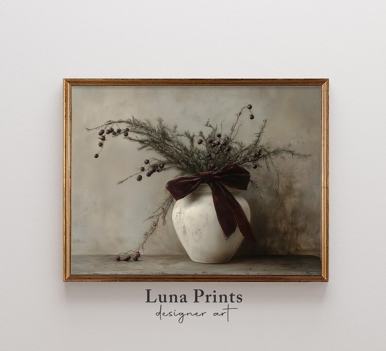 May include: A white ceramic vase with a burgundy velvet bow sits on a wooden surface. The vase is filled with dried branches with small, dark berries. The background is a light gray wall.