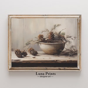 May include: A framed painting of a still life featuring a white bowl filled with pine cones and branches. The bowl is sitting on a wooden table with additional pine cones scattered around it. The background is a light beige wall.