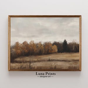 May include: A framed landscape painting in a gold-coloured frame. The artwork shows a field with trees in shades of brown and gold under a cloudy sky. The text "Luna Prints - designer art" is at the bottom.