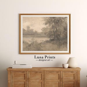 May include: A framed sepia-toned watercolor painting of a landscape with trees and a lake. The painting is in a wooden frame with a light brown finish. The painting is titled "Luna Prints - designer art".