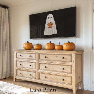 May include: A wooden dresser with six orange pumpkins of varying sizes on top. Above the dresser is a black television screen displaying a white ghost holding an orange pumpkin. The text "Luna Prints" is at the bottom of the image.
