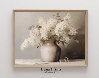 May include: A white ceramic vase filled with a bouquet of white flowers. The vase has a rustic, textured finish. The flowers are arranged in a loose, natural style. The background is a soft, neutral color.