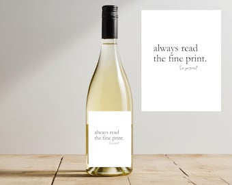 May include: A clear wine bottle with a black cap and a white label that reads "always read the fine print." A white card next to the bottle has the same text. The wine bottle is on a wooden surface.