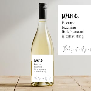 Puede incluir: Una botella de vino con tapón negro y etiqueta blanca. La etiqueta dice "wine. Porque enseñar a los pequeños humanos es agotador. Gracias por todo lo que haces." Una tarjeta blanca con el mismo texto está al lado.