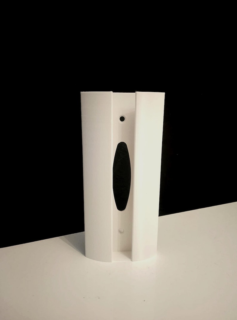 May include: White plastic wall mount with a slot for a dispenser. The mount has a small round hole and a larger oval hole.