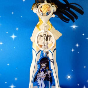 May include: A blue and white anime character keychain with a sword. The character has black hair and is wearing a white dress with a blue sash. The keychain is attached to a silver chain.