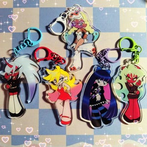 Puede incluir: Una colección de llaveros acrílicos con personajes de estilo anime. Cada llavero tiene un diseño único con colores vibrantes, incluyendo rojo, amarillo, azul y verde. Los llaveros están sujetos a cierres de varios colores.