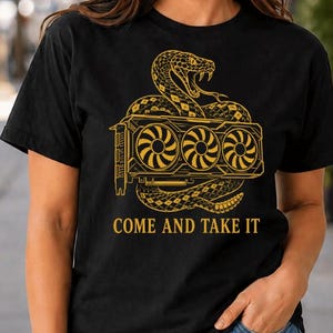 May include: A black short-sleeve t-shirt featuring a gold graphic of a coiled snake wrapped around a triple-fan graphics card. Below the illustration, the text reads COME AND TAKE IT in a bold, capitalized gold font centered on the chest.