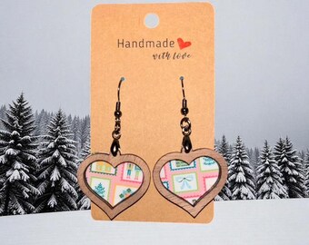 Puede incluir: Pendientes en forma de corazón con marco de madera y diseño estampado colorido. Los pendientes cuelgan de ganchos negros y se exhiben en una tarjeta marrón que dice "Handmade with love".