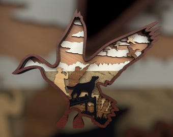 May include: A layered wooden art piece in the shape of a duck in flight. The artwork features a hunting scene with hunters, a dog, and flying ducks. The piece uses various wood tones and colors, including brown, white, and black.