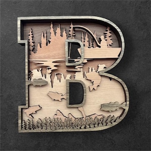 May include: Wooden letter "B" with a layered design featuring a fishing scene. The design includes a lake, trees, fish, and a person fishing from a boat. The letter is made of light and dark brown wood with a gray border.
