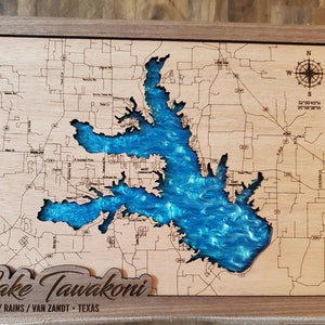 May include: A wooden map of Lake Tawakoni in Texas, with the lake filled in with blue resin. The map includes roads and other geographical features. The text "Lake Tawakoni" is carved into the wood below the map, along with the text "HUNT/RAINS/VAN ZANDT - TEXAS".
