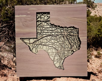 May include: A wooden wall art piece featuring a detailed map of Texas with roads and highways carved into the wood. The map is surrounded by a dark brown frame.