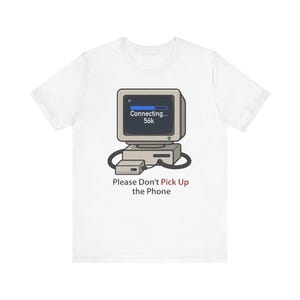 Peut inclure: T-shirt blanc avec un dessin d'ordinateur rétro affichant "Connecting... 56k". Le texte "Please Don't Pick Up the Phone" est en dessous. Le design est une référence humoristique à l'internet par modem et à l'ancienne technologie.