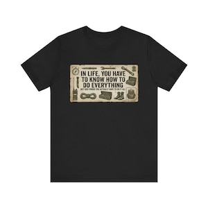 Puede incluir: Una camiseta negra de manga corta con un gráfico rectangular que contiene el texto "IN LIFE, YOU HAVE TO KNOW HOW TO DO EVERYTHING BUT GOD FORBID YOU ACTUALLY HAVE TO DO IT ALL" rodeado de ilustraciones de una brújula, cuchillo, llave y botas.