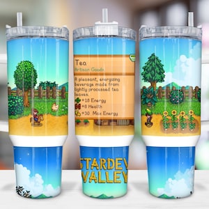 Könnte beinhalten: Ein Edelstahlbecher mit weißem Griff und Deckel. Der Becher zeigt ein Pixelbild eines Videospielcharakters, der auf einem Pferd in einem Feld mit blauem Himmel und weißen Wolken reitet. Der Text "STARDEW VALLEY" ist auf der Unterseite des Bechers aufgedruckt. Der Text "Tea Artisan Goods" ist zusammen mit einer Beschreibung des Tees auf der Seite des Bechers aufgedruckt.
