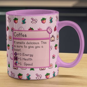Könnte beinhalten: Eine rosa Kaffeetasse mit einem pixeligen Design, das eine Kaffeetasse, Herzen und Hasen zeigt. Die Tasse hat einen rosa Henkel und ein weißes Inneres. Der Text auf der Tasse lautet "Coffee" und beschreibt die Vorteile des Kaffeetrinkens, darunter mehr Energie, Gesundheit und Geschwindigkeit.