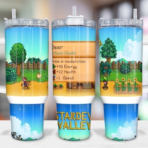 Könnte beinhalten: Ein Edelstahlbecher mit weißem Griff und einem Strohhalm. Der Becher zeigt ein Pixelbild eines Videospielcharakters, der auf einem Pferd in einem Feld mit blauem Himmel und weißen Wolken reitet. Der Text "Beer Artisan Goods" und "Stardew Valley" ist auf dem Becher sichtbar.