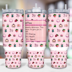 Könnte beinhalten: Ein rosafarbener Edelstahlbecher mit einem weißen Deckel und Griff. Der Becher zeigt ein pixeliges Design aus verschiedenen rosa und weißen Objekten, darunter ein Kuchen, eine Blume, ein Kaninchen und eine Erdbeere. Der Text "offee" ist auf dem Becher abgebildet, zusammen mit dem Text "smells delicious. This is sure to give you a boost. 1+3 Energy +1 Health +1 Speed".