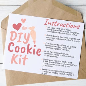 May include: A white card with pink hearts and the text "DIY Cookie Kit" in pink lettering. The card includes instructions for decorating cookies, such as letting the icing sit at room temperature, kneading the icing bags, and cutting a small tip off the icing bag.
