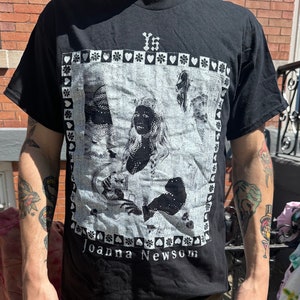 Może przedstawiać: Czarny T-shirt z białym nadrukiem graficznym przedstawiającym kobietę z długimi włosami i tekstem "YS" i "Joanna Newsom".
