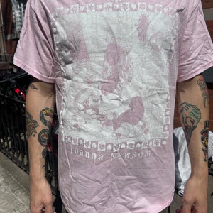 Może przedstawiać: R&oacute;żowy t-shirt z białym nadrukiem graficznym przedstawiającym kobietę z koroną i tekstem "YS" i "Joanna Newsom".