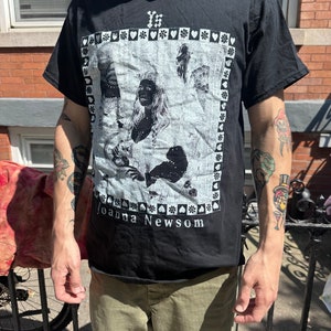 Może przedstawiać: Czarny T-shirt z białym nadrukiem przedstawiającym twarz kobiety i tekst "Joanna Newsom".