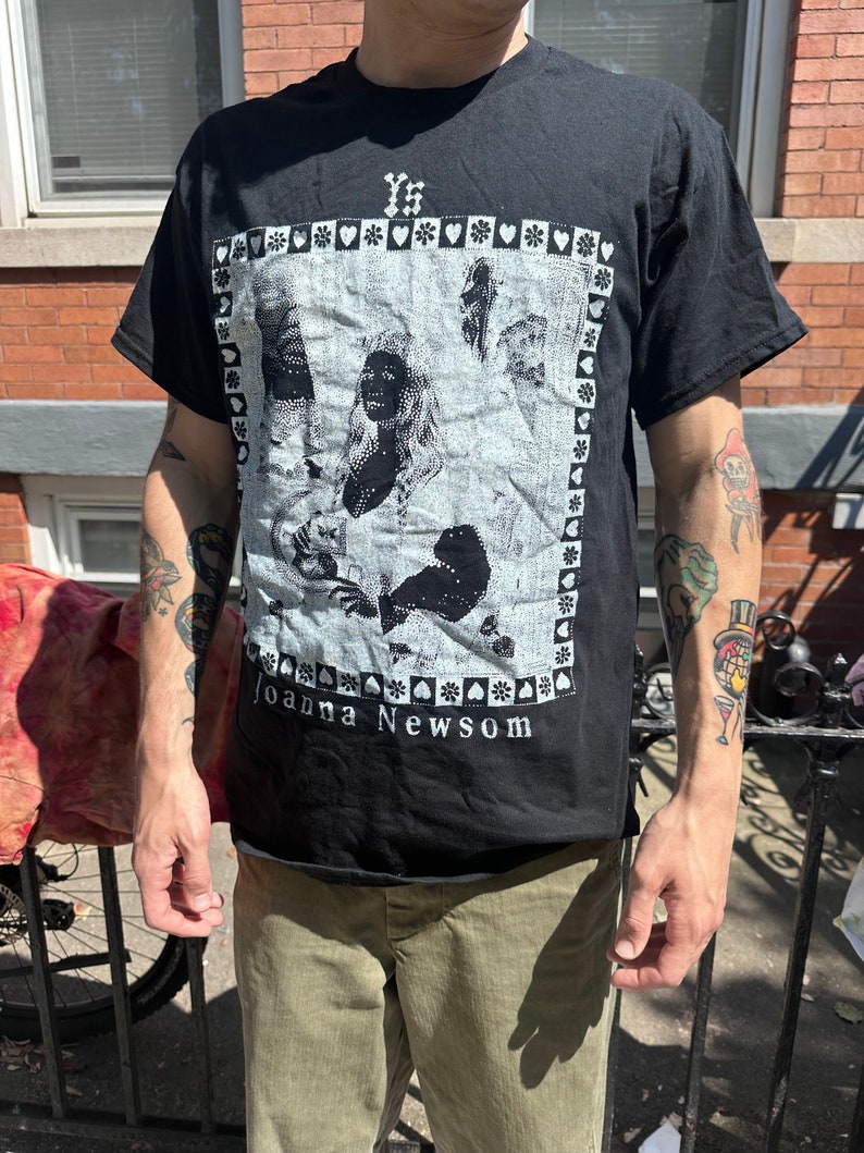 Może przedstawiać: Czarny T-shirt z białym nadrukiem przedstawiającym twarz kobiety i tekst "Joanna Newsom".