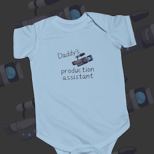 May include: Light blue baby onesie with the text "Daddy's production assistant" and a cartoon image of a video camera.