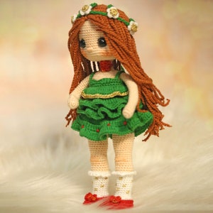 May include: A crocheted doll with long, brown hair, wearing a green dress with gold trim and a white flower crown.