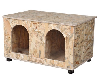 May include: A wooden double-door pet house with a light brown finish. The house has two arched entrances and a flat roof. The house is sitting on four black legs. The house has the word "habitevi" printed on the front.