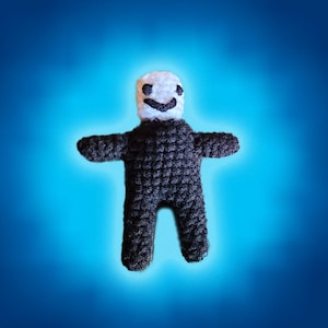 May include: A black crocheted plush toy with a white smiling face. The toy has a simple design with arms and legs.